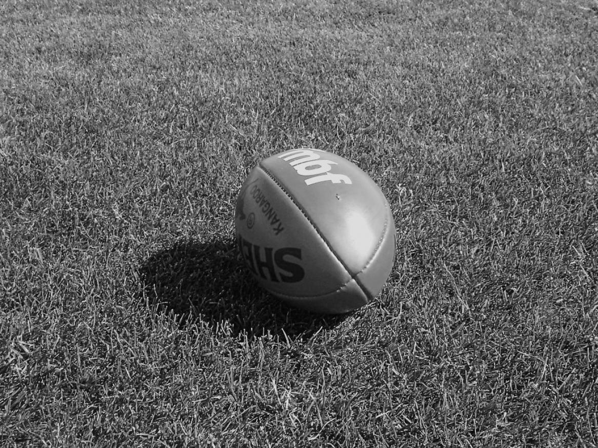 Black and white image of aussie rules football ball on grass