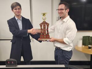 Ilya and Bryce shake hands and hold the Lorne Neudorf Cup 