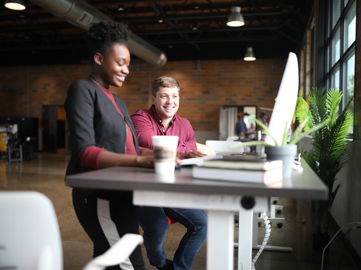 Colleagues stand and look at a computer, smiling