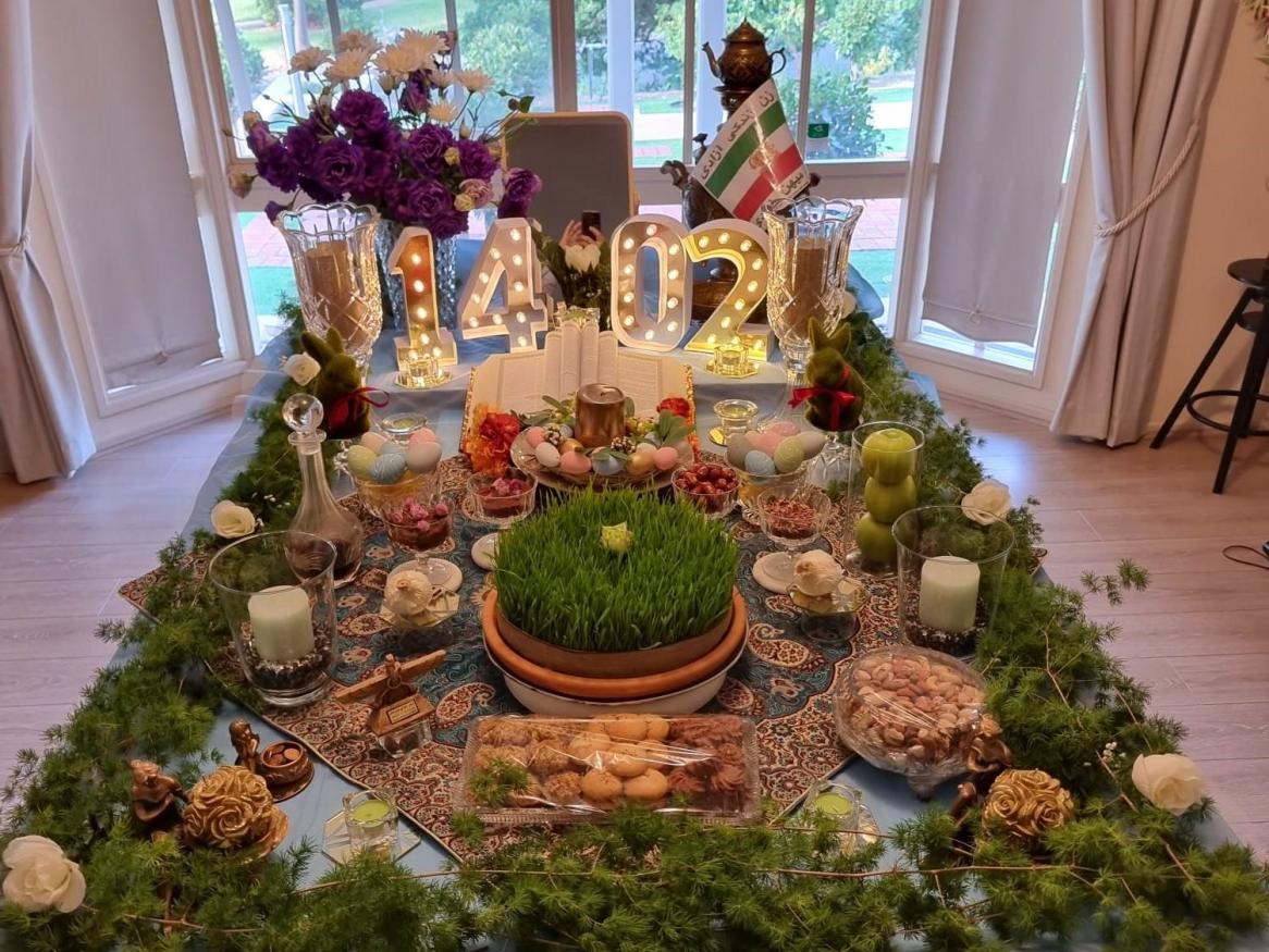 A haft-sin table is covered in food, lights, and a Persia flag.