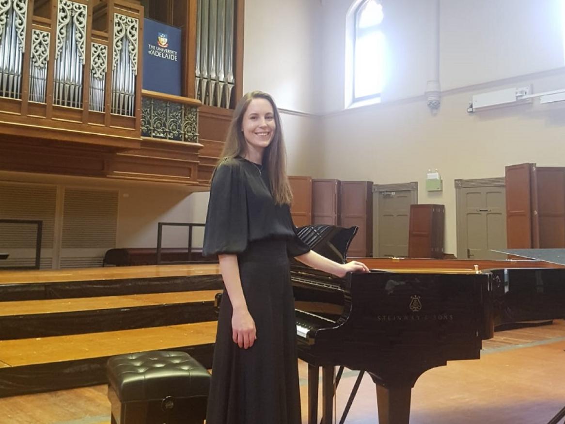Anne Mathews standing alongside piano in Elder Hall