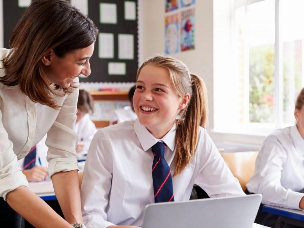 A teacher helps a smiling student on a laptop